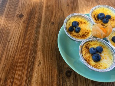 Turkuaz bir tabakta folyo kalıplı yaban mersinli puding ve ahşap bir masada turuncu fizsalis. Boşluğu kopyala