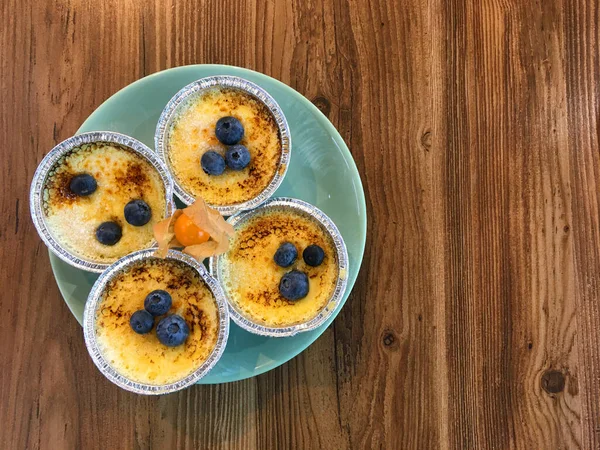 Turkuaz bir tabakta folyo kalıplı yaban mersinli puding ve ahşap bir masada turuncu fizsalis. Boşluğu kopyala