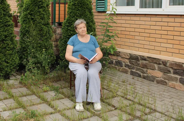 Una Anciana Está Sentada Patio Día Verano Leyendo Libro Veces — Foto de Stock