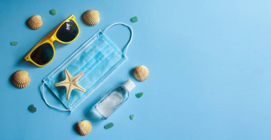 Yaz 2020 konsepti. Seyahat, tatil ve Coronavirus ve diğer enfeksiyonlara karşı koruma. Koruyucu tek kullanımlık maske, güneş gözlüğü, antiseptik, deniz yıldızı ve deniz kabukları. Pankart