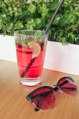 Limonata, nane yaprağı, uzun ve berrak bir bardakta buz küpleri ve güneş gözlüğünün yanındaki masada duran tüplerle ferahlatıcı limonata. Dinlenme, dikkat dağıtma, rahatlama kavramı.
