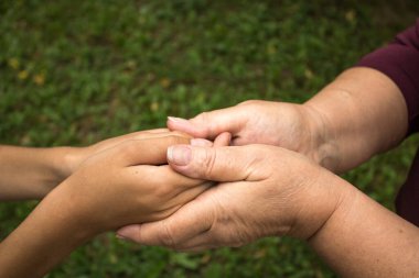 Büyükannenin elleri, küçük bir çocuğun elini yeşil çimen arka planında tutuyor. Nesiller arasında sevgi ve arkadaşlık kavramı. Uluslararası Yaşlılar ve Büyükbabalar Günü