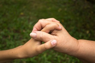 Bir büyükanne ve küçük bir çocuk yeşil çimenlerin arka planında el ele tutuşuyorlar. Nesiller arasında sevgi ve arkadaşlık kavramı. Uluslararası Yaşlılar ve Büyükbabalar Günü