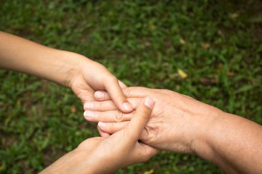 Çocuğun elleri nazikçe büyükannenin ellerini yeşil çimlerin arka planında tutuyor. Nesiller arasında sevgi ve arkadaşlık kavramı. Ulusal Yaşlılar ve Büyükbabalar Günü