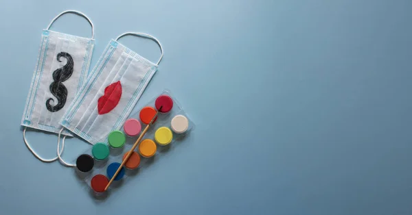 Tek kullanımlık bıyıklı maskeler ve çocuk tarafından çizilmiş dudaklar büyük anne ve babaya hediye olarak ya da renkli boyaların yanında duran aileler için. Mavi arka plan. Uluslararası Yaşlılar ve Büyükbabalar Günü. Yaşlılar için bakım kavramı. Pankart