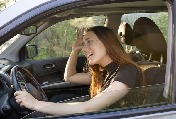 Stresli, kızıl saçlı genç kadın sürücü arabasında oturuyor ve diğer sürücülere küfrediyor. Trafik sıkışıklığı kavramı. 