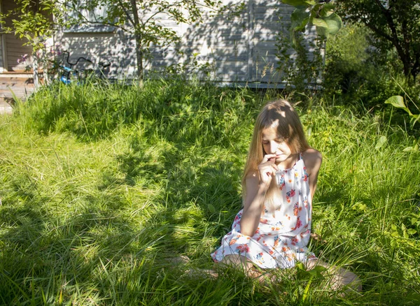 ブロンドの女の子は目を閉じて庭の明るい緑の芝生の上に座っています 彼女は太陽と夏を楽しむ 幸せな子供時代 晴れた夏 楽しい思い出と感情の概念 — ストック写真