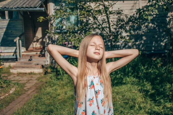 Altın saçlı kız, ılık yaz güneşinin altında parlak yeşil yaprakların arasında güneşleniyor. Mutlu çocukluk kavramı, güneşli yaz, sonbahar, hoş anılar ve duygular.