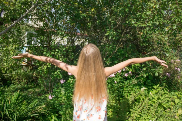 Altın saçlı kız kollarını açık yeşil yapraklara ve çimenlere doğru açtı. Mutlu çocukluk kavramı, güneşli yaz, sonbahar, hoş anılar ve duygular.
