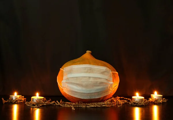 Cadılar Bayramı balkabağı, siyah arka planda yanan mumların yanında tek kullanımlık koruyucu bir maskenin içinde. Coronavirus 'un koşullarında Cadılar Bayramı kutlaması için hazırlık kavramı. Boşluğu kopyala