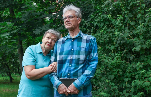 Yaşlı bir çift parkta yeşil yapraklı bir arka plana karşı duruyor. Uluslararası Yaşlılar ve Büyükbabalar Günü