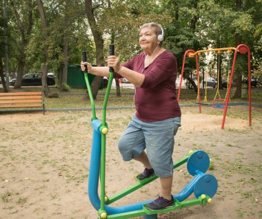 Yaşlı kadın spor eğitmeni Elips üzerinde egzersiz yapıyor. Bahçede antrenman. Mutlu yaşlılık ve vücut pozitifliği kavramı. Uluslararası Yaşlılar ve Büyükbabalar Günü