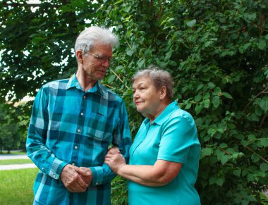 Mutlu yaşlı çift parkta yeşil yapraklı bir arka planda duruyor. Uluslararası Yaşlılar ve Büyükbabalar Günü