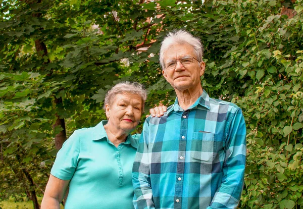 Mutlu yaşlı çift parkta yeşil yapraklı bir arka planda duruyor. Uluslararası Yaşlılar ve Büyükbabalar Günü