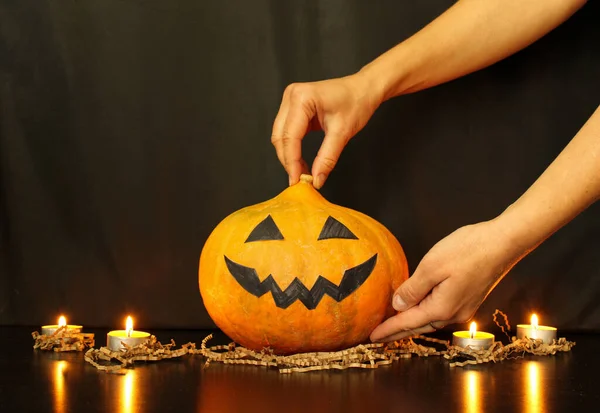 Mother\'s hands put a pumpkin with a face made by child on the table. The child\'s hand gives a burning candle. Process of decoration of home for Halloween party.