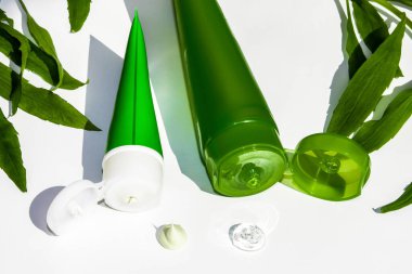 Beyaz arka planda krema için iki tüp. Yeşil yaprakların arasında. Beyaz arka planda krema ve jöle