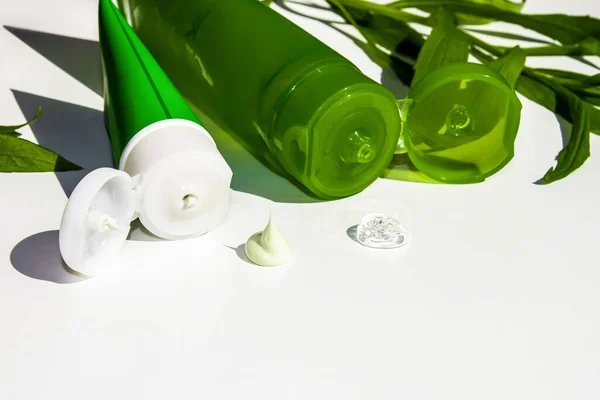 Two tubes for cream on a white background. Among the green leaves. Cream and gel on a white background