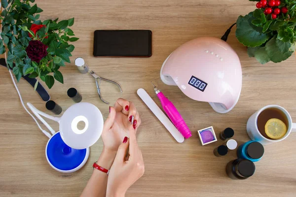 Kız manikür aletiyle tırnaklarını tedavi ediyor. Tırnak cilası, manikür aletleri. Ultraviyole lamba. Evde manikür..