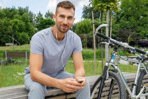 A man listens to music with headphones. There is a bicycle nearby.