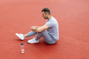 Bir adam parkta oturur ve müzik dinler..