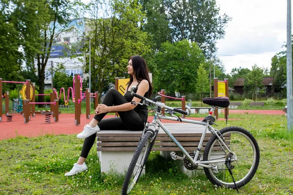 The girl is resting on the sports ground. There is a bicycle nearby.