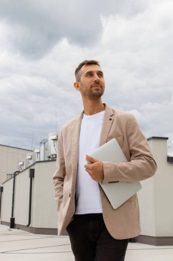 Ceketli bir adam dizüstü bilgisayar tutuyor..