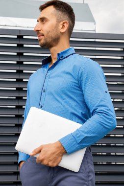 Mavi gömlekli genç bir adam dizüstü bilgisayar tutuyor..