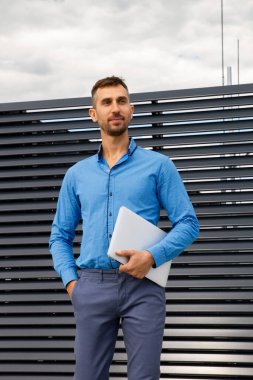 Mavi gömlekli genç bir adam dizüstü bilgisayar tutuyor..