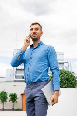 Mavi gömlekli genç bir adam telefonda konuşuyor..