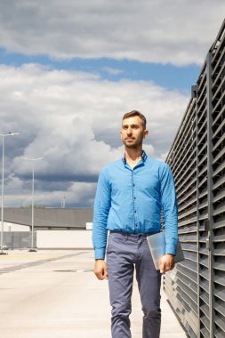 Mavi gömlekli genç bir adam dizüstü bilgisayar tutuyor..