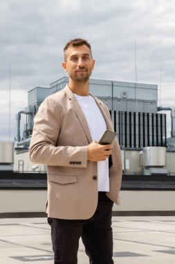 Ceketli bir adam elinde telefon tutuyor..