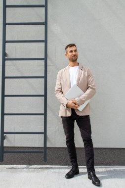 Dizüstü bilgisayarı olan bir adam merdivenlerin yanında duruyor..