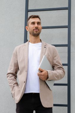 Dizüstü bilgisayarı olan bir adam merdivenlerin yanında duruyor..