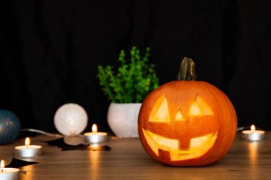 Yüzü oyulmuş bir balkabağı. Mumların yanında, siyah bir arka planın arkasında..