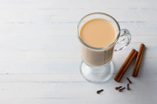 Spicy warming tea with milk in a glass cup with cinnamon sticks and cloves