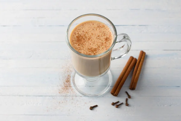 Spicy warming tea with milk in a glass cup with cinnamon sticks and cloves