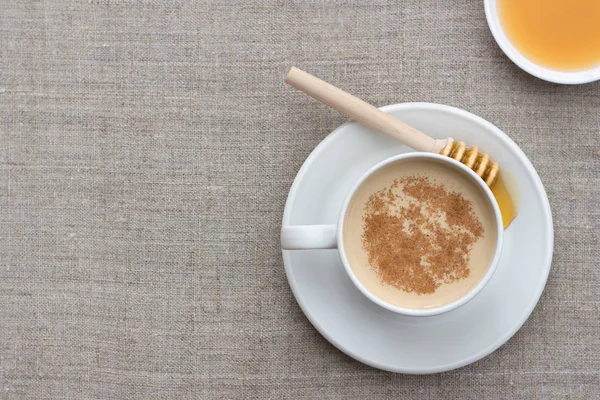 Spicy warming tea with milk in white porcelain cup with honey on textile background