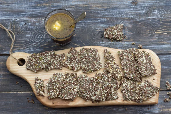 Delicious healthy multigrain gluten-free crackers, ketogenic, from chia seeds, flax, sesame and ground pumpkin seeds on wooden board and keto coffee in glass with spoon of butter on wooden table