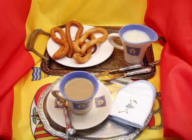 Tipik İspanyol churro 'larıyla nefis bir kahvaltı, iki gümüş tepsiyle, bardakla kahve setiyle, sütle, çatal bıçakla, İspanya bayrağında, ürün fotoğrafıyla.,