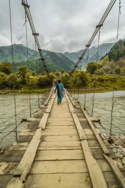 Pakistan 'da tehlikeli görünen köprüden Indus nehrinden geçen bir kadın..