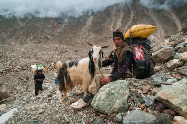 Karakoram, Pakistan - 24 Temmuz 2018: Şerpa ve bir keçi Pakistan 'daki Karakoram Dağları' ndaki K2 ana kampına giderken dinleniyor. İllüstrasyon Editörü.