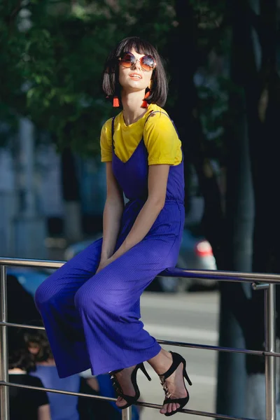 Bright summer trend. Fashion portrait of stylish young woman with trendy haircut and sunglasses wearing yellow t-shirt and violet denim. Summer fashion trend.