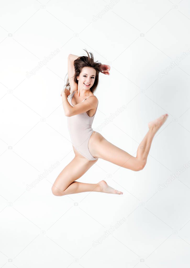 Beautiful woman with perfect slim body and long legs jumping - fitness concept. Happy and smiling young girl over white background.