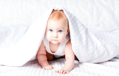 Cute, komik küçük bebek beyaz örtünün altında gülümseyerek. Kopya alanı