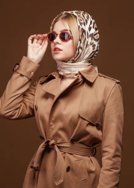 Moda trendy trençkot genç şık kadın portresi, leopar baskı headdress ve moda güneş gözlüğü bej renkli arka plan üzerinde.