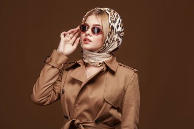 Moda trendy trençkot genç şık kadın portresi, leopar baskı headdress ve moda güneş gözlüğü bej renkli arka plan üzerinde.