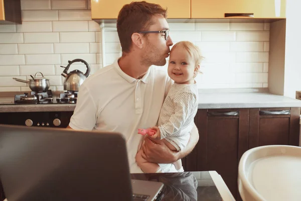 Happy young father working on laptop at home with little baby da