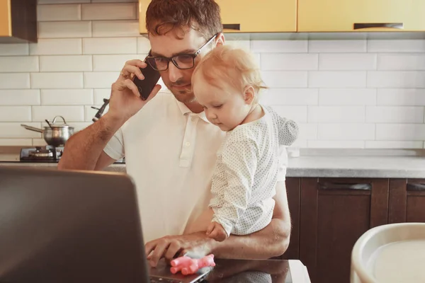 Padre de familia trabaja con un ordenador portátil a través de Internet, hablando phon — Foto de Stock