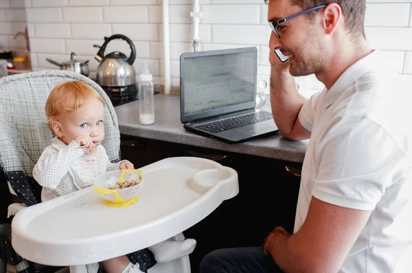 Lycklig ung pappa arbetar hemma och sitter med en baby girl. — Stockfoto