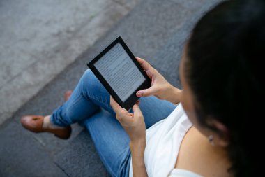 Genç Latin kadın dijital tablet cihazıyla kitap okuyor. Kitaba odaklan..